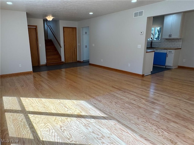 spare room with a textured ceiling, light wood-style flooring, visible vents, baseboards, and stairs