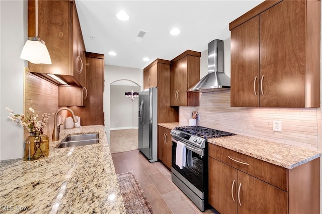 kitchen featuring backsplash, light stone countertops, appliances with stainless steel finishes, wall chimney exhaust hood, and a sink