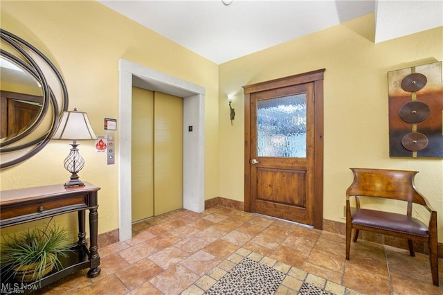 entrance foyer with elevator, baseboards, and stone tile flooring