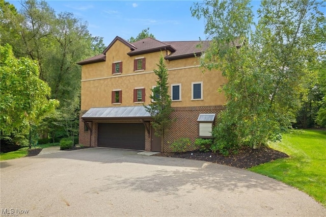 view of front facade with an attached garage, stucco siding, a front lawn, aphalt driveway, and brick siding