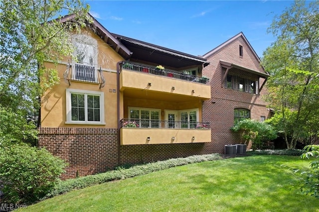 back of house featuring brick siding, a balcony, a yard, and stucco siding