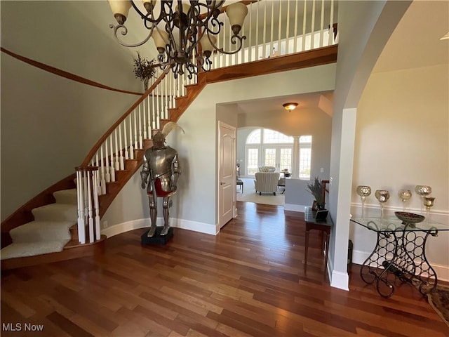 foyer featuring baseboards, arched walkways, stairway, wood finished floors, and a high ceiling