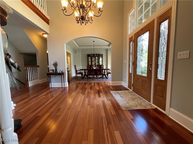 foyer with hardwood / wood-style flooring, baseboards, a chandelier, and arched walkways