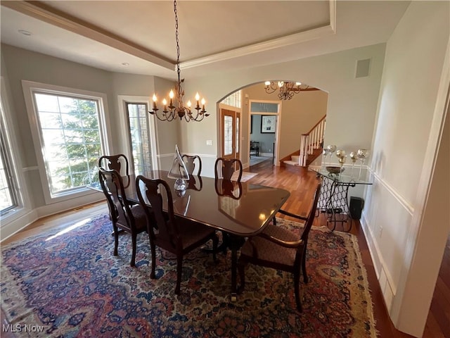 dining space with arched walkways, a tray ceiling, wood finished floors, and visible vents