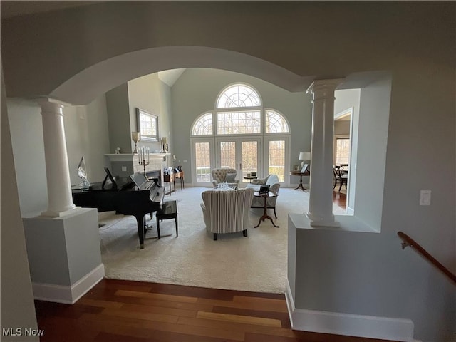 living area featuring arched walkways, decorative columns, vaulted ceiling, wood finished floors, and baseboards