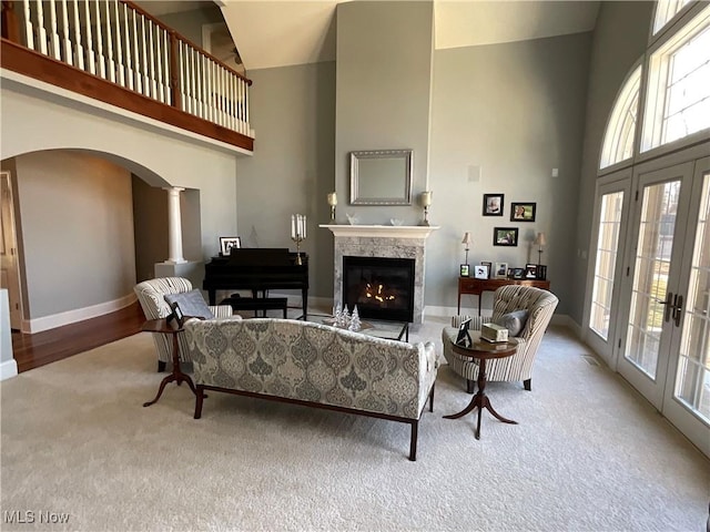 carpeted living room featuring a high end fireplace, ornate columns, french doors, and a high ceiling