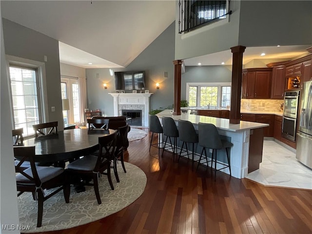 dining area featuring light wood-type flooring, ornate columns, a wealth of natural light, and a glass covered fireplace