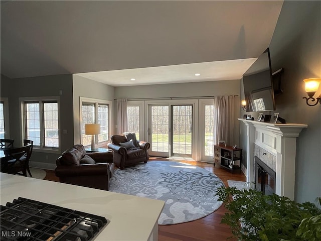 living area featuring baseboards, a glass covered fireplace, lofted ceiling, wood finished floors, and recessed lighting