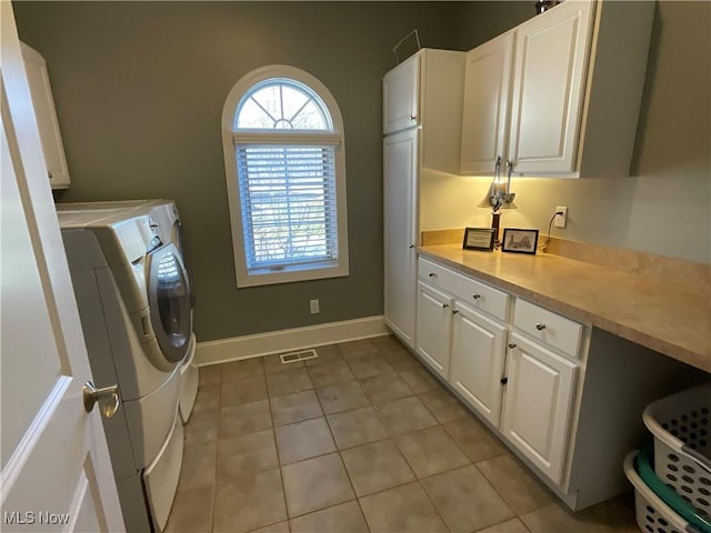 clothes washing area with washing machine and clothes dryer, light tile patterned floors, cabinet space, visible vents, and baseboards