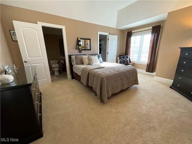 bedroom with light carpet, a spacious closet, baseboards, and vaulted ceiling