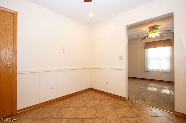 unfurnished room featuring tile patterned flooring, wainscoting, and ceiling fan