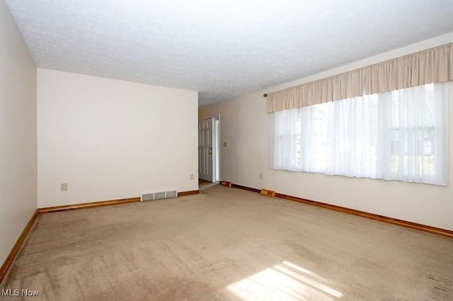 carpeted empty room featuring visible vents, a textured ceiling, and baseboards