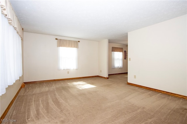 unfurnished room featuring light carpet and baseboards