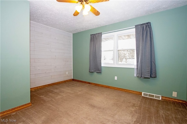 carpeted spare room featuring wooden walls, baseboards, visible vents, a ceiling fan, and a textured ceiling