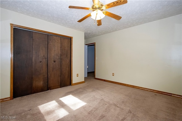 unfurnished bedroom featuring a closet, light colored carpet, a ceiling fan, a textured ceiling, and baseboards