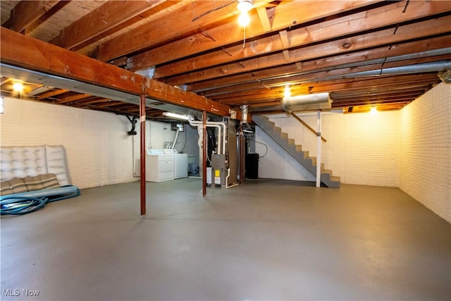 unfinished below grade area with stairs, brick wall, washing machine and dryer, and heating unit