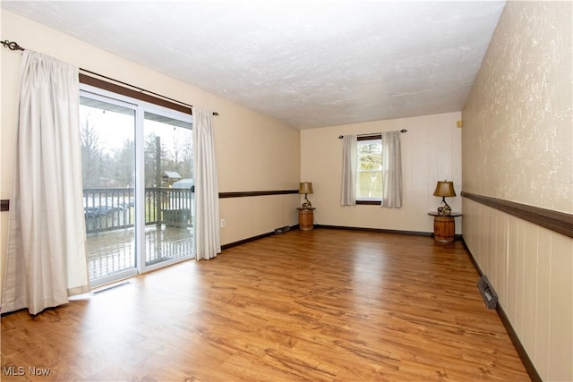 spare room featuring light wood-style floors, visible vents, a textured ceiling, and a textured wall