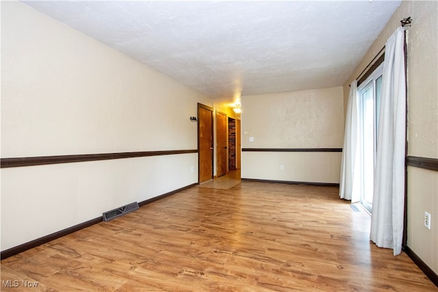 empty room with baseboards, visible vents, a textured ceiling, and light wood finished floors