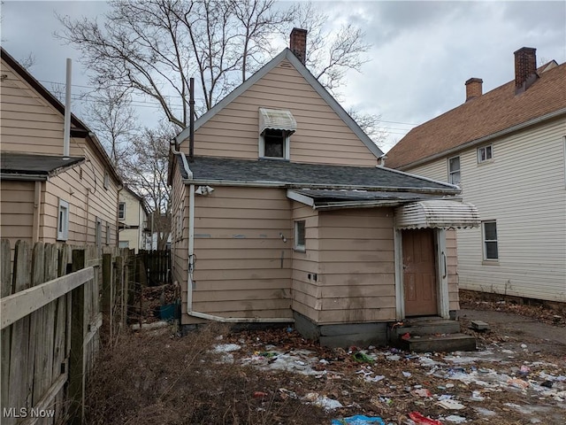 rear view of property featuring a shingled roof, entry steps, and fence