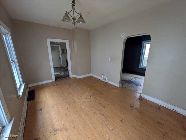 unfurnished dining area with arched walkways, wood finished floors, visible vents, baseboards, and an inviting chandelier