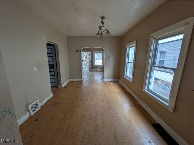 unfurnished dining area featuring light wood-type flooring, visible vents, arched walkways, and baseboards