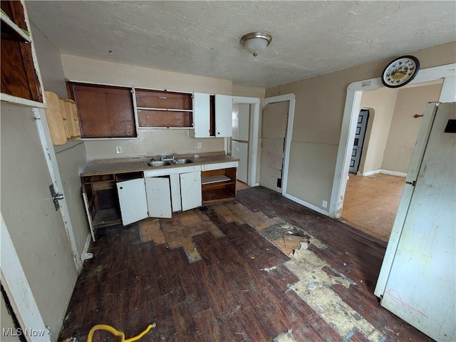 kitchen with dark wood-type flooring, freestanding refrigerator, a textured ceiling, open shelves, and a sink