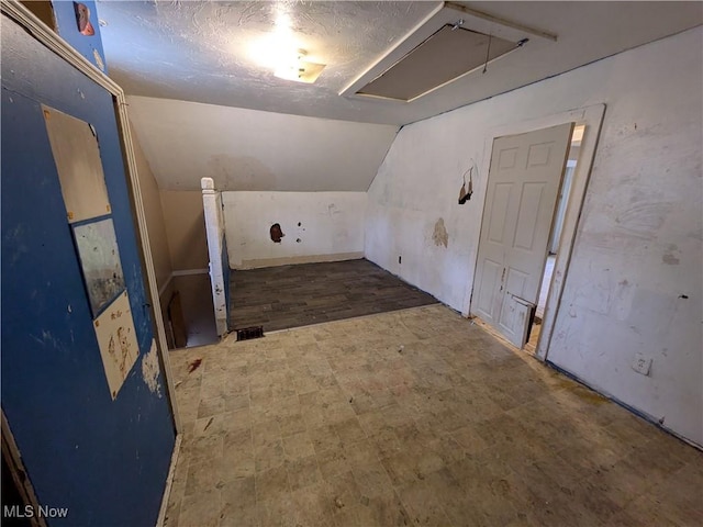 bonus room featuring attic access, vaulted ceiling, and a textured ceiling