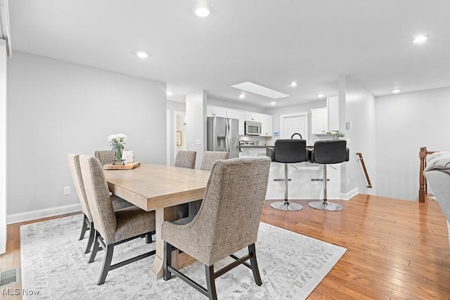 dining area featuring a skylight, light wood-style flooring, baseboards, and recessed lighting