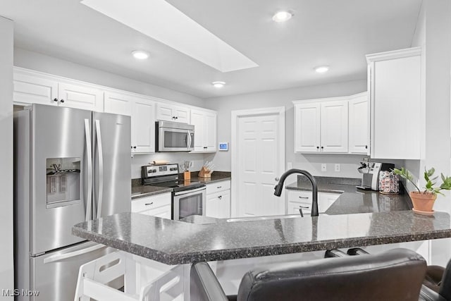 kitchen featuring a peninsula, a skylight, appliances with stainless steel finishes, and white cabinets