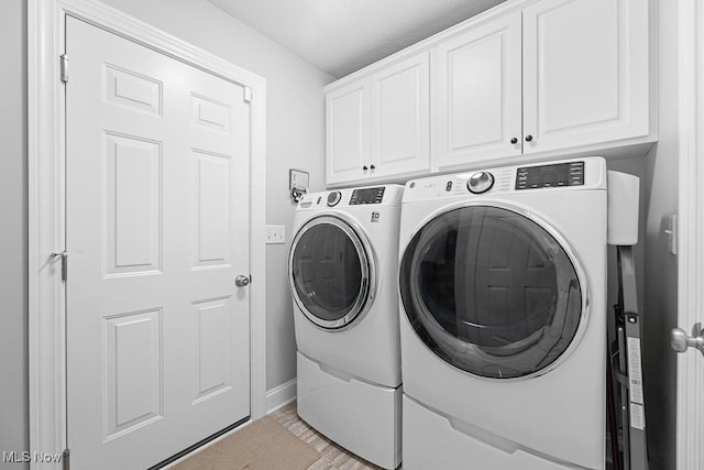 clothes washing area with light wood-style flooring, washing machine and clothes dryer, cabinet space, and baseboards