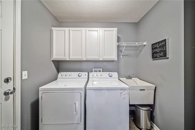 laundry area featuring washing machine and clothes dryer, cabinet space, a sink, a textured ceiling, and baseboards