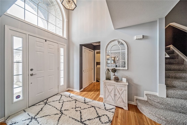 foyer entrance featuring a textured ceiling, stairs, baseboards, and wood finished floors