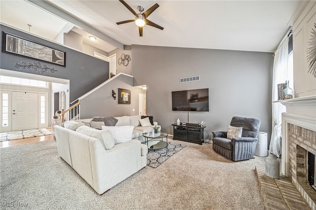 living area with a fireplace, visible vents, stairway, a ceiling fan, and high vaulted ceiling