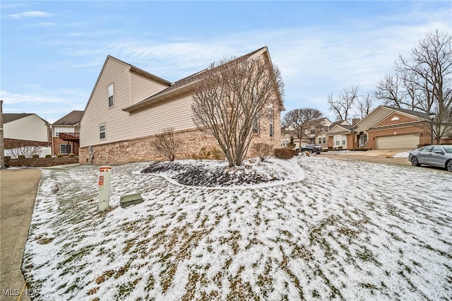 snow covered property with a garage, a residential view, and brick siding