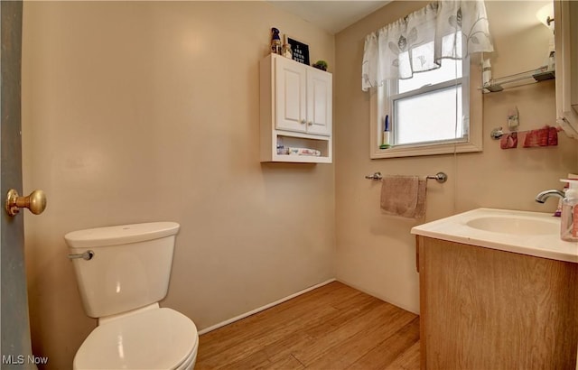 half bathroom with toilet, wood finished floors, and vanity