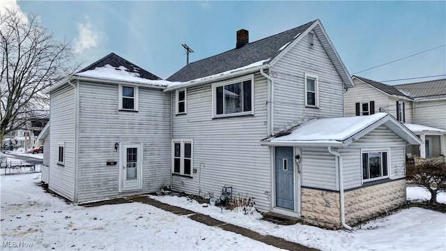 snow covered back of property featuring a chimney