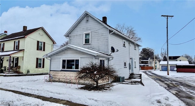 view of snowy exterior with an outbuilding, a chimney, and a detached garage