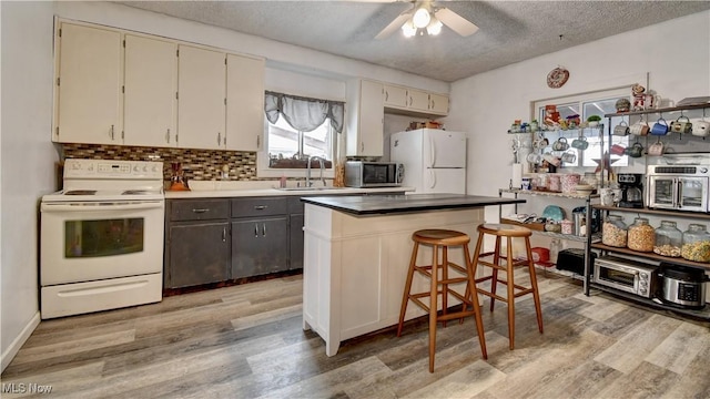 kitchen featuring light wood finished floors, white appliances, a textured ceiling, and a sink