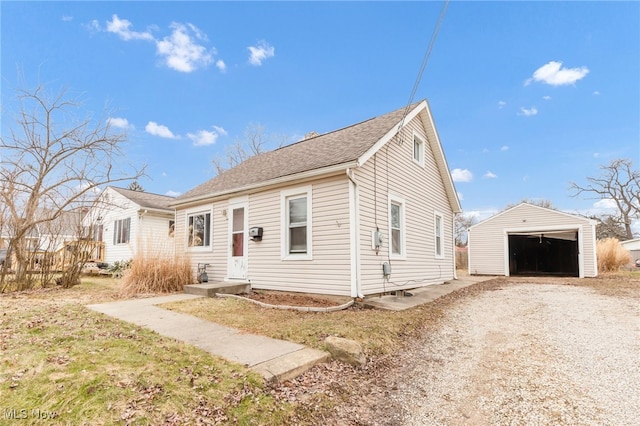 view of front of house with a garage, driveway, roof with shingles, and an outdoor structure