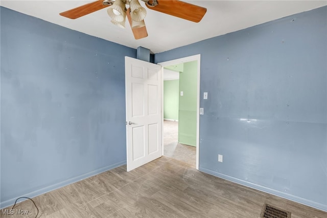 empty room featuring a ceiling fan, wood finished floors, visible vents, and baseboards