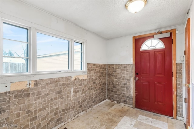 entrance foyer featuring a wainscoted wall, tile walls, and a textured ceiling