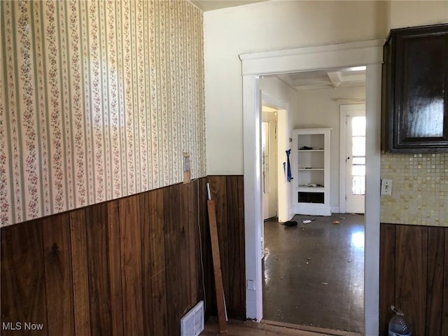 hallway with a wainscoted wall, wood walls, visible vents, and beamed ceiling