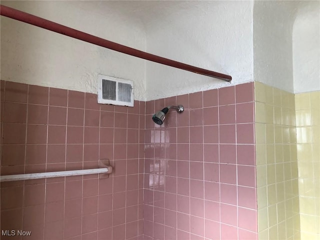 interior space with a textured wall, tiled shower, and visible vents