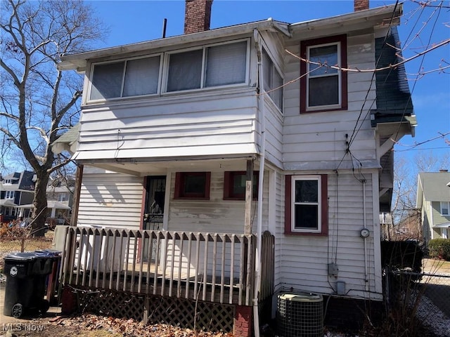 rear view of house with central AC, a porch, a chimney, and fence