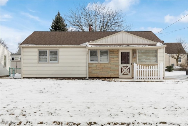 bungalow featuring stone siding, fence, and roof with shingles