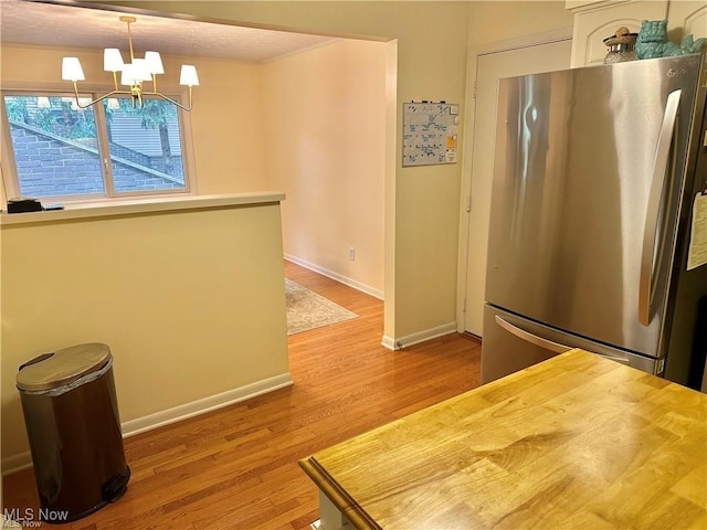 kitchen featuring baseboards, wood finished floors, freestanding refrigerator, wooden counters, and a notable chandelier