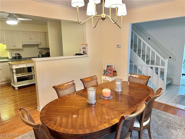 dining area featuring ceiling fan with notable chandelier, crown molding, light wood-style flooring, and stairs