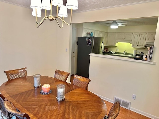 dining area featuring ceiling fan with notable chandelier, baseboards, visible vents, and crown molding