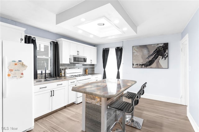 kitchen with white appliances, a raised ceiling, a sink, and white cabinets