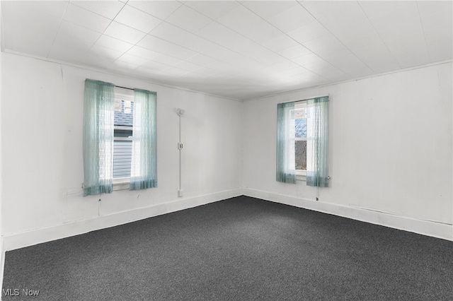 empty room with plenty of natural light, dark carpet, and baseboards